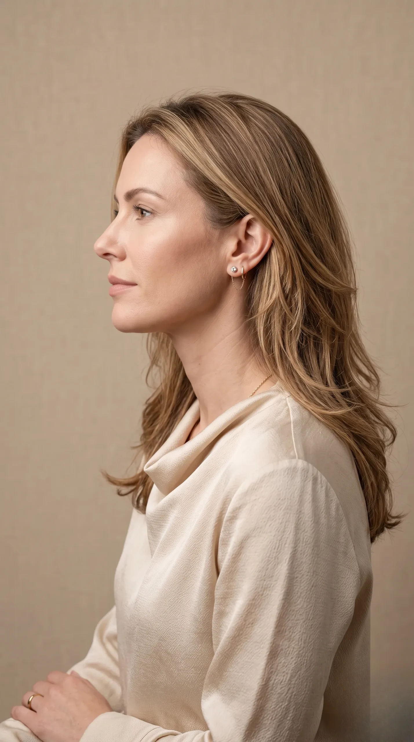 Profil d'une femme avec une coupe mi-longue dégradée, lumière douce sur fond beige neutre.