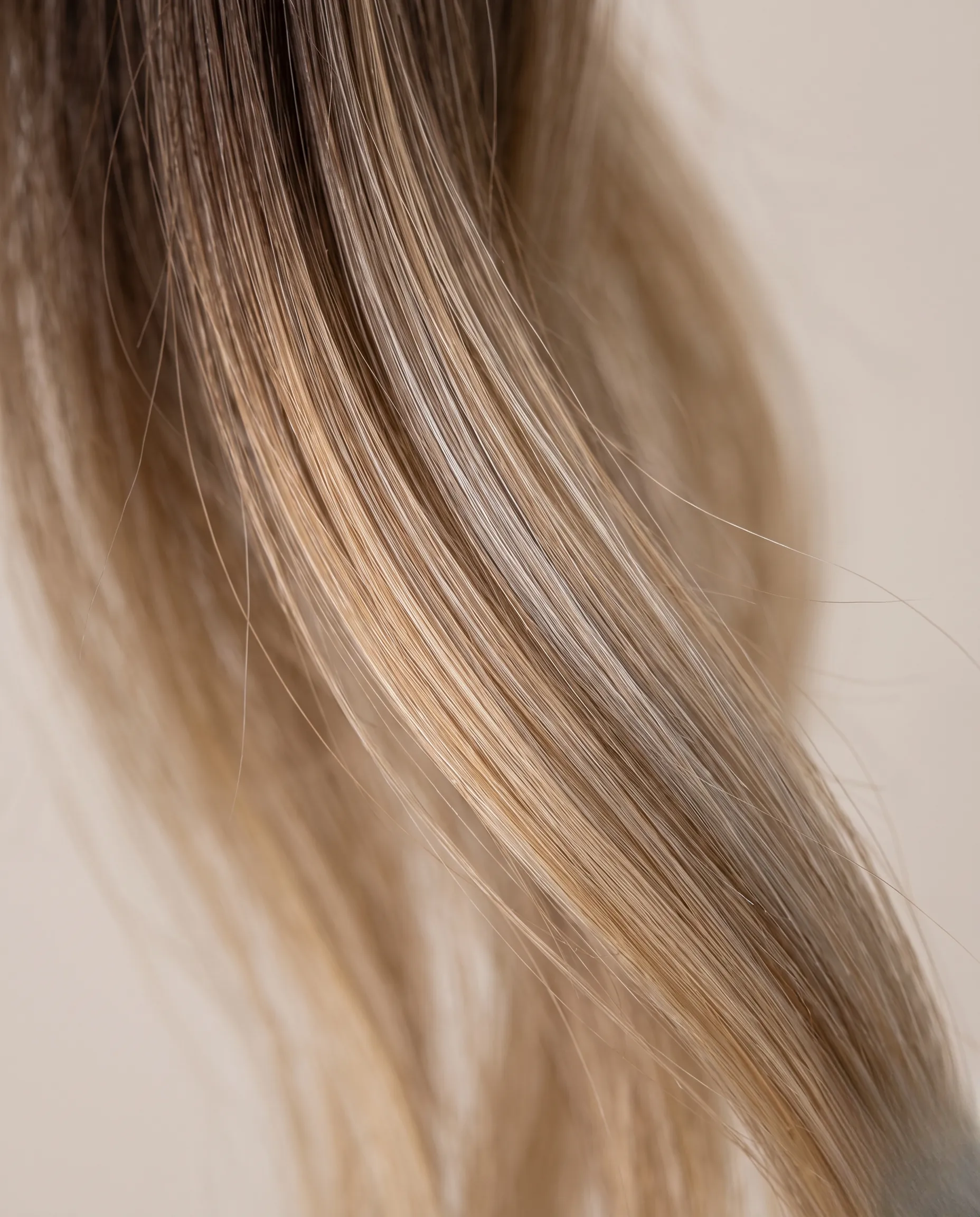 Gros plan macro sur la texture brillante et les nuances d'un balayage blond parfaitement fondu.